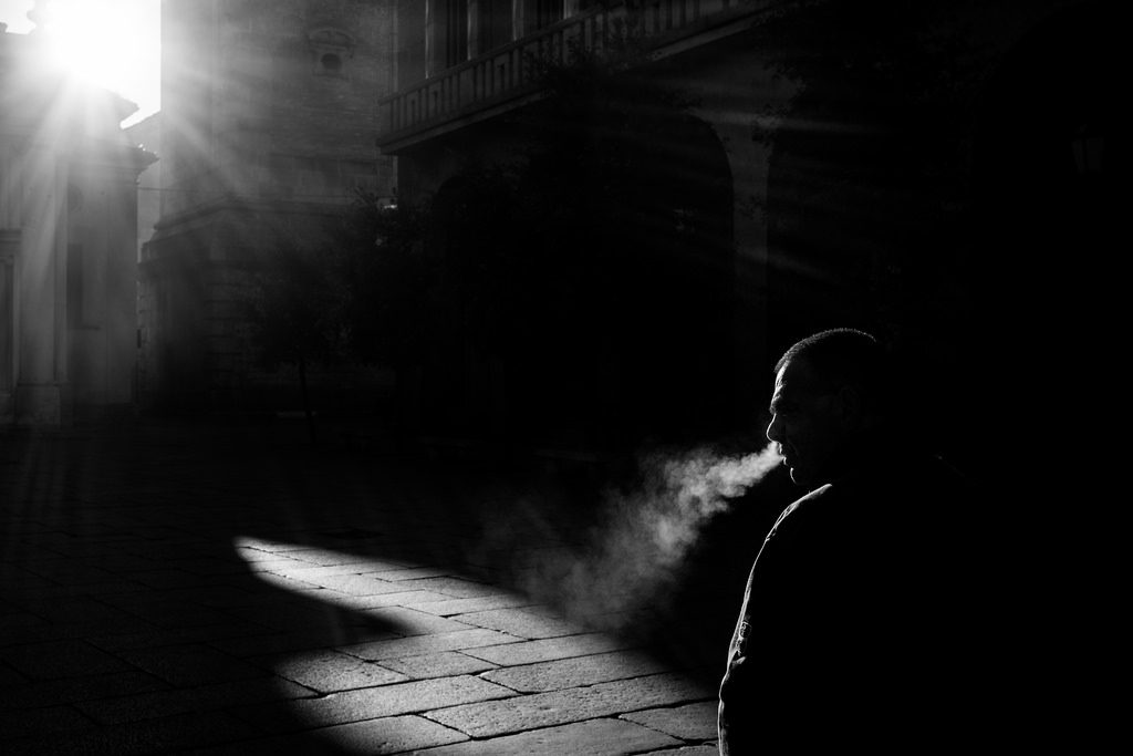 picture of man in shadows in a street, smoking
