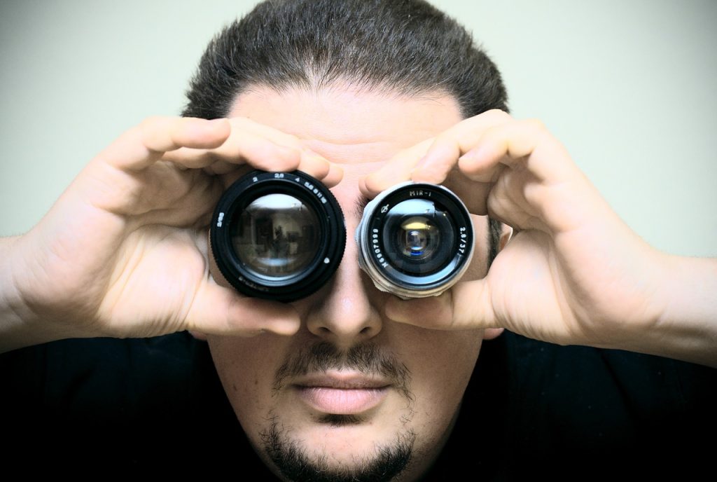 man holding camera lenses in front of each of his eyes so they look like his eyes